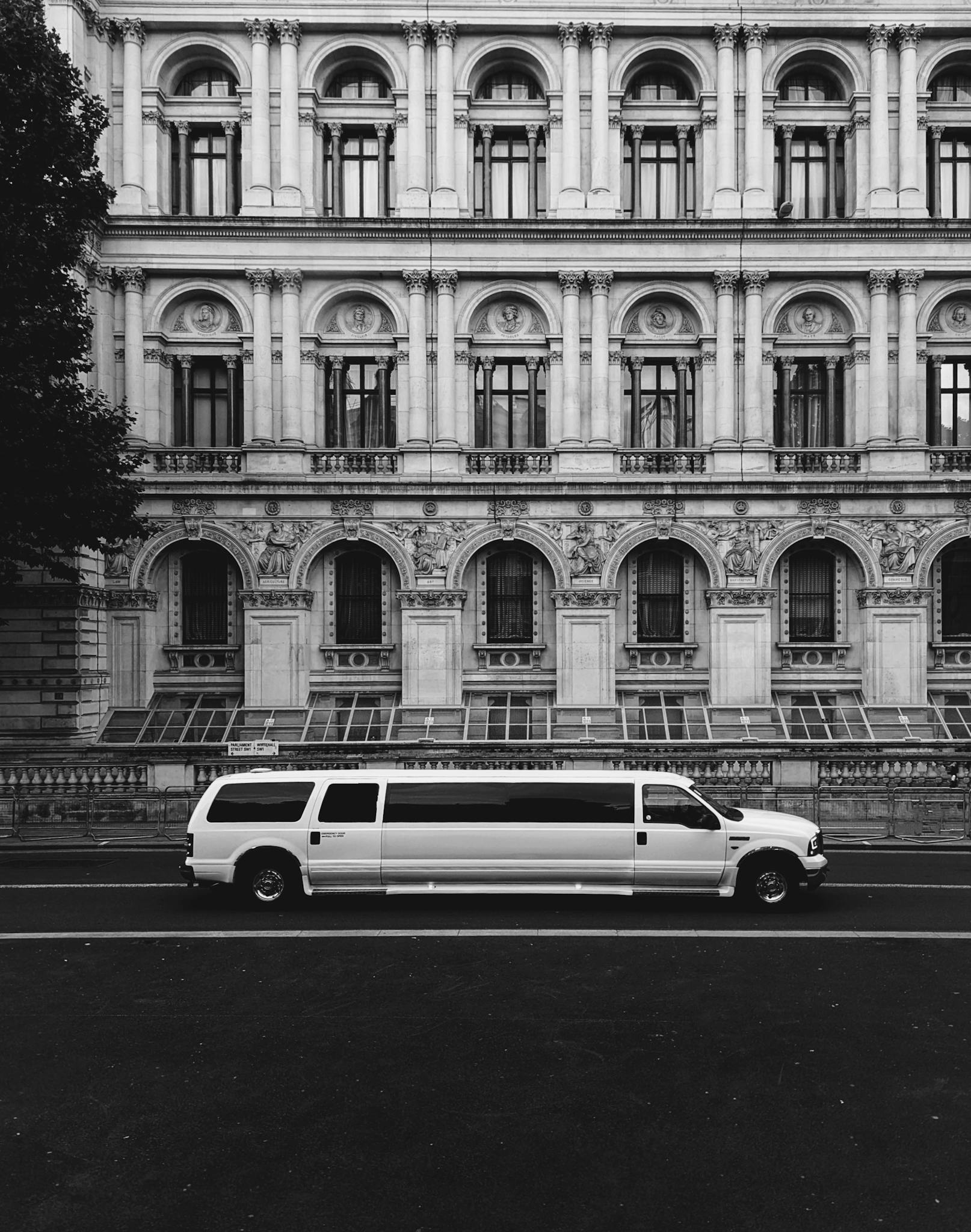 A white limousine parked in front of a historic building in London, showcasing architectural elegance.