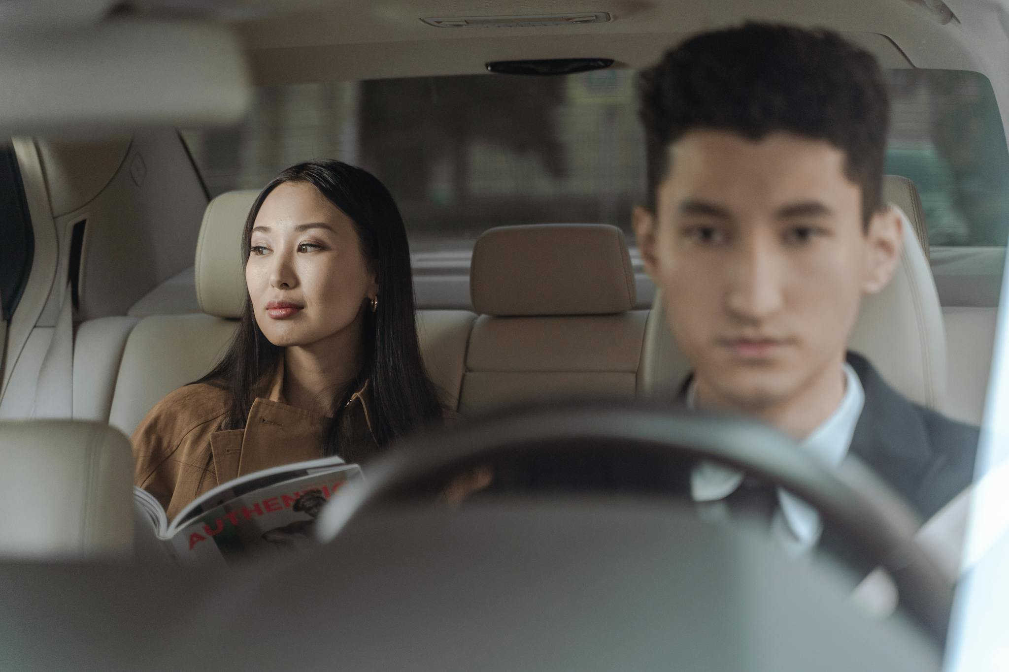 Asian businesswoman and male chauffeur in a luxury car interior, representing travel comfort and professional transportation.