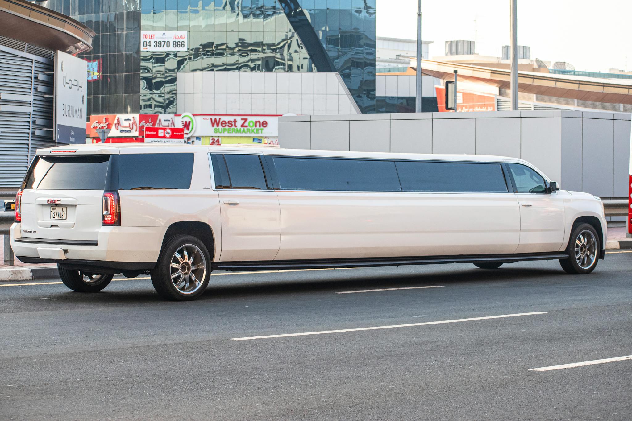 White GMC Yukon XL limousine parked on a bustling city street during the day.